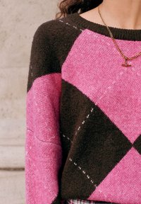 Strickpullover mit einem rosafarbenen und braunen Rautenmuster, geripptem Halsausschnitt und weicher Textur. Eine goldene Kettenhalskette fügt ein Detail hinzu.