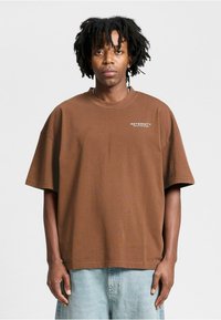 Brown cotton t-shirt with a relaxed fit, short sleeves, and a crew neck. Features white text logo on the left chest area.