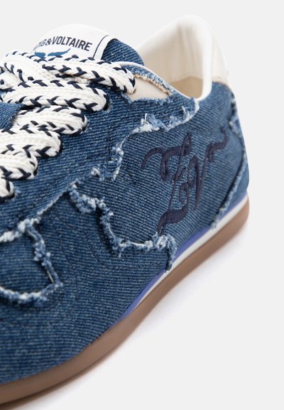 Μπλε τζιν αθλητικό παπούτσι με λευκά και μαύρα πλεγμένα κορδόνια, ξεφτισμένα άκρα, κεντημένη λεπτομέρεια κειμένου και μπεζ περιθώριο σόλας.