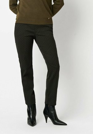 Schwarze, taillierte Hosen mit einem vertikalen Muster, aus strukturiertem Stoff, kombiniert mit spitzen, schwarzen Ankle-Boots. Akzentuiert durch dezente Details.