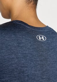 Αθλητικό πουκάμισο σε ναυτικό μπλε με στρογγυλή λαιμόκοψη και υφασμάτινη υφή. Διαθέτει λευκό λογότυπο στο πίσω μέρος κοντά στον γιακά.