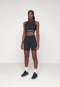 Black Nike Pro sports crop top and shorts, featuring a branded elastic band. Model wears black athletic shoes and white socks.