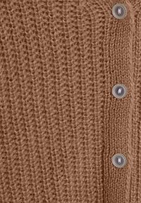 Brun stickad cardigan med en texturerad ribbdesign, försedd med stora, genomskinliga knappar framtill för stängning.