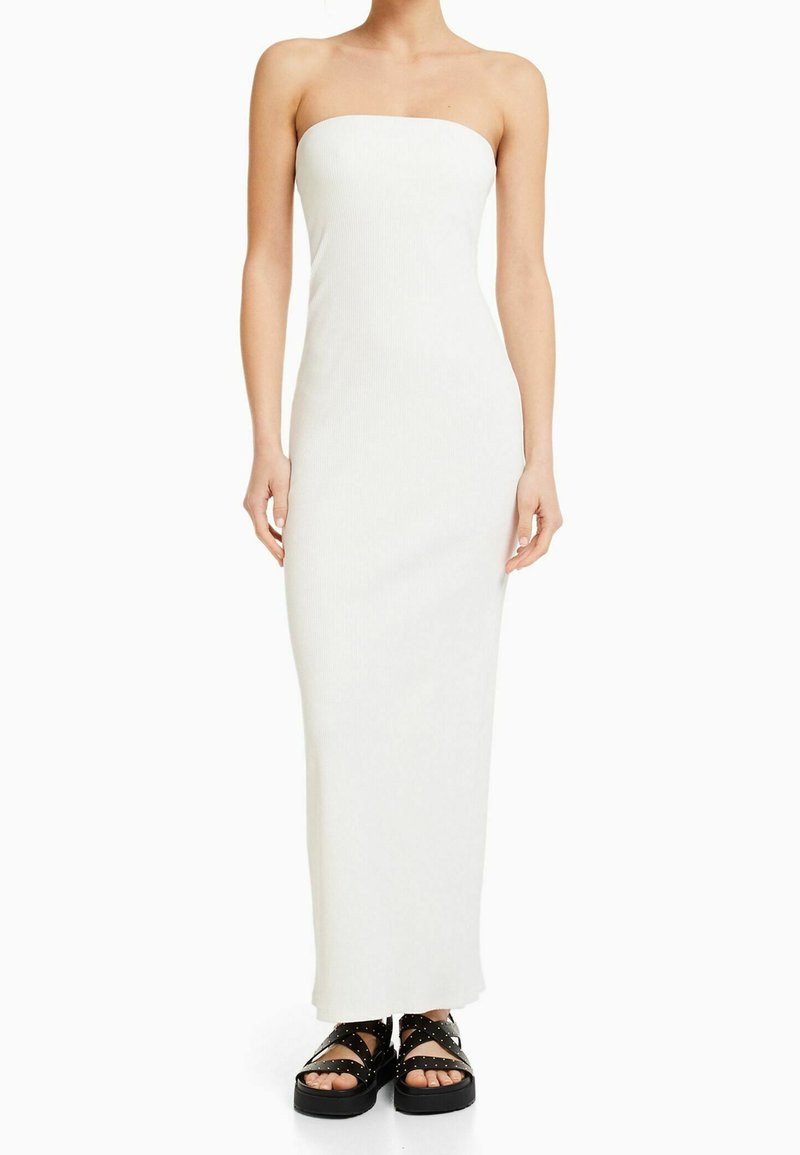 Witte, strapless, geribbelde maxi-jurk met een nauwsluitende silhouet. Gecombineerd met chunky zwarte sandalen met gestudde accenten.