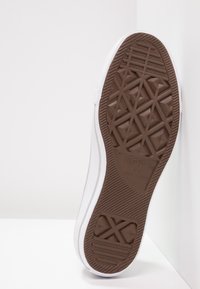 Vita canvas sneakers med en brun gummisula. Sulan har ett diamantmönster och ett präglat varumärkeslogotyp. Visad i sidovy.