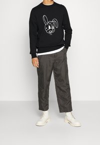 Felpa nera con una grafica di un coniglio bianco, abbinata a pantaloni striped grigi e stivali in pelle color crema con lacci.