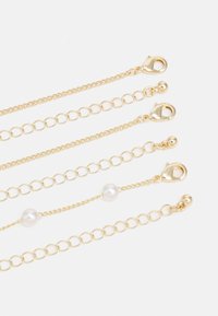 Goldene Kettenglieder mit verschiedenen Designs, die glatte Perlen und Verschlüsse aufweisen. Ein Strang enthält Perlenakzente.