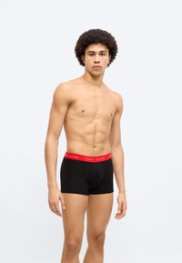 Μαύρα ανδρικά σορτς μποξέρ με κόκκινη μέση που φέρει το λογότυπο «TOMMY HILFIGER», βαμβακερό μείγμα, μήκος μέχρι το μέσο μηρού, εφαρμοστό σχέδιο.