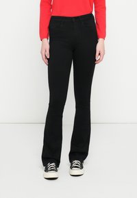 Czarne rozszerzane jeansy wykonane z elastycznego denimu, posiadające klasyczny fason z pięcioma kieszeniami i przeszyciami, w połączeniu z czarnymi sneakersami.
