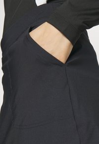 Černé sportovní kalhoty s elegantním designem, které mají boční kapsu a hladký, pružný materiál. Šité akcenty zajišťují vyšší odolnost.