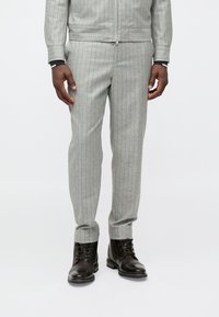 Siva trenirka z drobnimi črtami, narejena iz teksturirane tkanine, v kombinaciji s črnimi usnjenimi škornji. Ozek kroj z zadrgo.