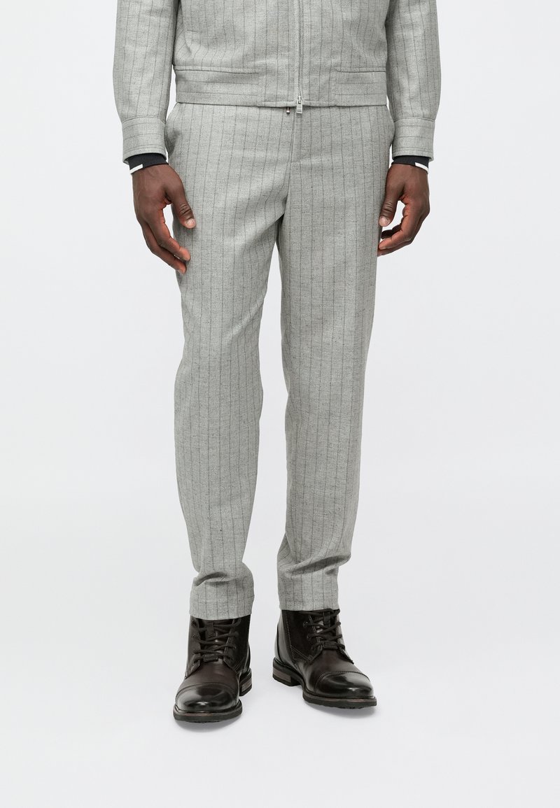 Siva trenirka z drobnimi črtami, narejena iz teksturirane tkanine, v kombinaciji s črnimi usnjenimi škornji. Ozek kroj z zadrgo.