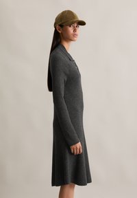 Abito a coste grigio scuro con maniche lunghe e colletto, caratterizzato da un design svasato. Abbinato a un cappello in velluto a coste marrone chiaro.
