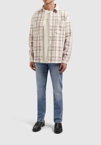 Geruite button-up shirt in beige en bruintinten, gelaagd over een licht crèmekleurig T-shirt. Draagt het met lichtblauwe rechte jeans en zwarte instappers.