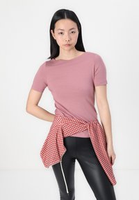 Pink short-sleeve t-shirt with a rounded neckline, paired with a red and white gingham check shirt tied at the waist, complemented by black leggings.