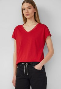 T-shirt rouge à manches courtes avec un col en V orné de dentelle. Fabriqué en matériau doux, associé à un pantalon noir et une ceinture à cordon décorative.