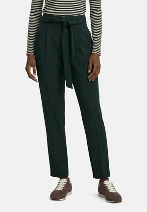 Personne portant un pantalon taille paperbag noir avec ceinture nouée, une chemise rayée à manches longues, et des baskets marron avec des lacets blancs.