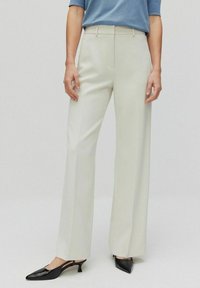 Vidbyxor i ett ljust beige tyg med en slät yta och sidfickor, kombinerade med svarta pumps med spetsig tå.