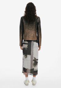 Robe longue et transparente avec un imprimé graphique de plantes en noir et blanc. Veste marron texturée à manches longues. Baskets blanches et chaussettes.