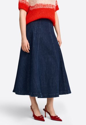 Donkerblauwe spijkerrok tot op de knie met paneelnaden, gedragen met rode hooggehakte slingbacks en een rood-witte gebreide trui.