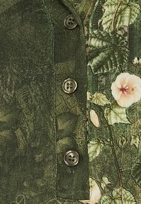 Mørkegrønt stof med et botanisk print, der viser blade og lyserøde blomster, placeret ved siden af fire blanke, runde knapper på en beklædningsplade.