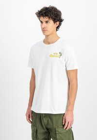 Hvid bomulds t-shirt med korte ærmer, der har en gul og grøn "Hawaii" grafisk tryk på venstre bryst. Enkel rund hals design.