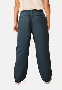 Nohavice so širokými nohavicami z tmavomodrej látky, s elastickým pásom, dvoma zadnými vreckami a hladkou matnou textúrou.