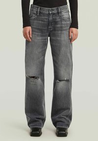 Jeans wide-leg in denim grigio con strappi e rotture, design a cinque tasche, cuciture a contrasto e orli dritti; indossati con scarpe nere.