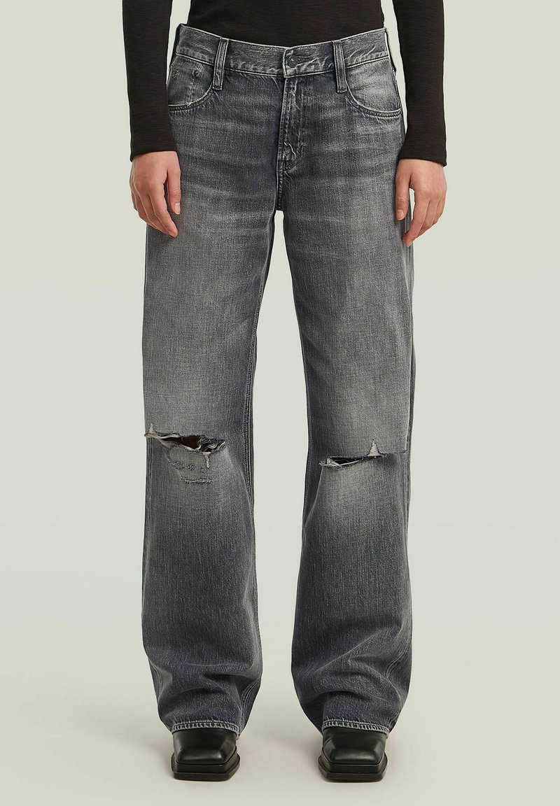 Jeans wide-leg in denim grigio con strappi e rotture, design a cinque tasche, cuciture a contrasto e orli dritti; indossati con scarpe nere.