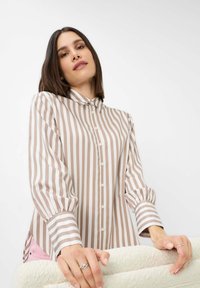 Blusa a maniche lunghe a righe beige e bianca. Presenta un colletto, una chiusura a bottoni e maniche a palloncino. Tessuto liscio con una texture leggera.