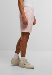 Lyserosa shorts med elastisk midje, sidelommer og avslappet passform, parret med off-white sneakers og ankelstående sokker.