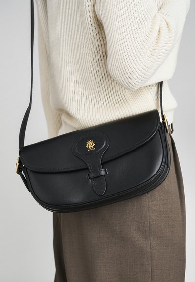 Black leather crossbody bag with a curved flap, gold logo accent, and a long adjustable strap. Smooth texture and minimalistic design.