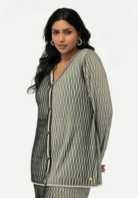 Musta ja kermanvärinen kuviollinen neuletakki v-pääntiellä, nappikiinnityksellä ja pitkällä hihalla. Sisältää ribbitekstuuri ja koristeellisia nappeja.