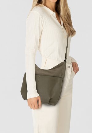 Dunkelgrüne Leder-Umhängetasche mit strukturierter Oberfläche, verstellbarem Tragegurt und flachem Design, gehalten von einer Person, die ein weißes Oberteil und eine Hose trägt.