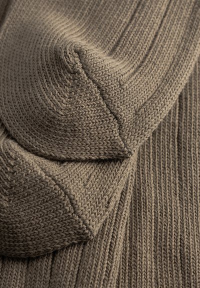 Gros plan sur un tissu tricoté marron côtelé plié avec des coutures visibles détaillées et une texture apparente.