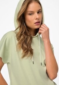 Světle zelená mikina s kapucí má ribbovanou strukturu a krátké rukávy. Nastavitelné šňůrky s kovovými konci. Měkká tkanina, ležérní design.
