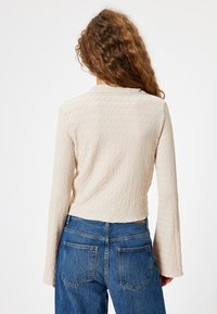 Beige strukturierter Langarm-Pullover mit Kragen und leicht verkürztem Schnitt, kombiniert mit blauen Jeans.