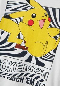 Geltona medvilnės marškinėliai su piešiniu Pikachu, turinčiu raudonus skruostus, ant balto fono. Juodai baltos spiralės raštai kaip akcentai.