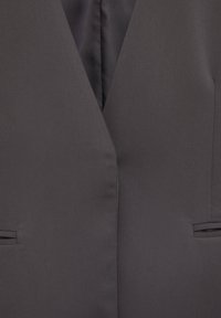 Blazer gris foncé avec revers et deux poches passepoilées horizontales, fabriqué en tissu tissé lisse.