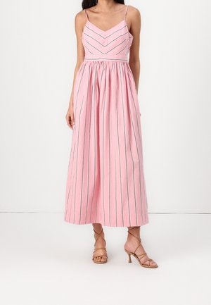 Mujer con un vestido midi sin mangas rosa con tirantes finos y rayas negras verticales, combinado con sandalias de tacón con tiras en color marrón claro.