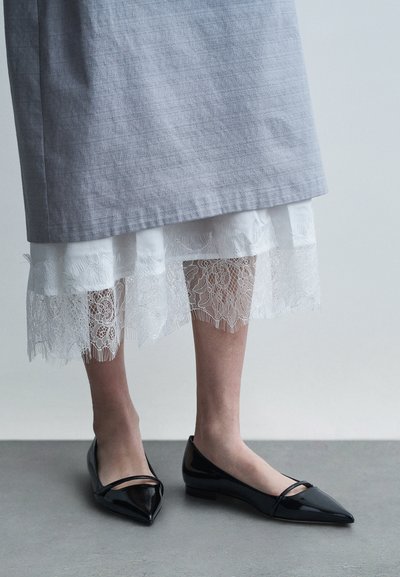 Grijze linnen rok over een witte slip met kanten rand, gecombineerd met glanzende zwarte spitse ballerina's. Het contrast in textuur tussen de materialen is opvallend.