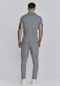 Šedý vzorovaný dvoudílný outfit skládající se z přiléhavého polo trička s límečkem a odpovídajících zúžených kalhot. Tričko obsahuje decentní značkování.