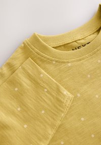 Light yellow t-shirt featuring a textured fabric with small white polka dots. Round neck and short sleeves with a stitched hem.