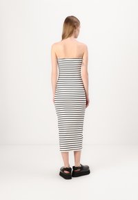 Vestido midi listrado em preto e branco, ajustado, com design de top tubo, textura canelada. Combinado com sapatos plataforma grossos pretos.