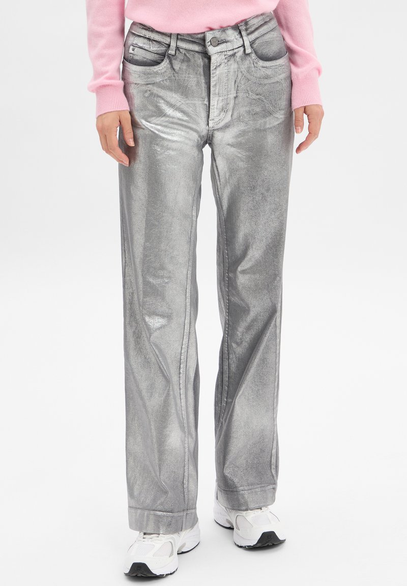 Jeans larges en métal argenté avec une surface texturée, des poches avant et une fermeture à bouton, associés à des baskets blanches.