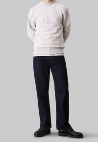 Sudadera gris claro con el logo "Calvin Klein Jeans", combinada con vaqueros de pierna recta de color azul oscuro y zapatos negros. Conjunto sencillo y casual.