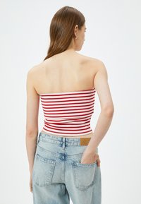 Top corto sin tirantes con rayas horizontales rojas y blancas, textura acanalada. Combinado con unos jeans de cintura alta en azul claro que tienen bolsillos traseros.
