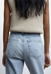 Los jeans de mezclilla azul claro cuentan con una cintura alta, dos bolsillos traseros con un diseño clásico y una parte superior de punto beige con textura que se usa por encima.