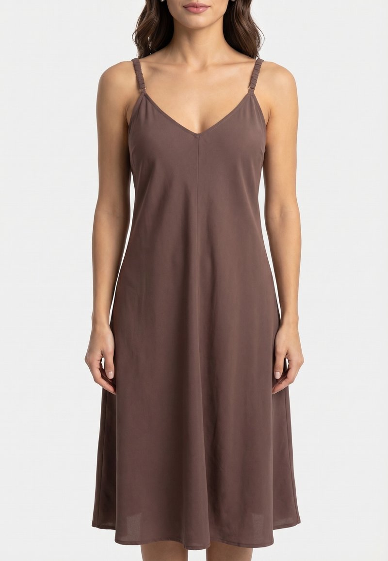 Femme portant une robe midi marron sans manches avec un décolleté en V et des bretelles spaghetti réglables, debout sur un fond blanc uni.