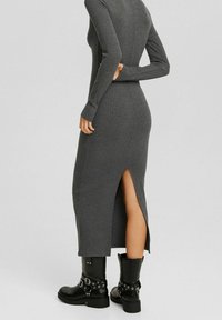 Abito grigio a maniche lunghe con costine e spacco laterale, realizzato in tessuto testurizzato. Abbinato a stivali neri al ginocchio con dettagli in fibbia.
